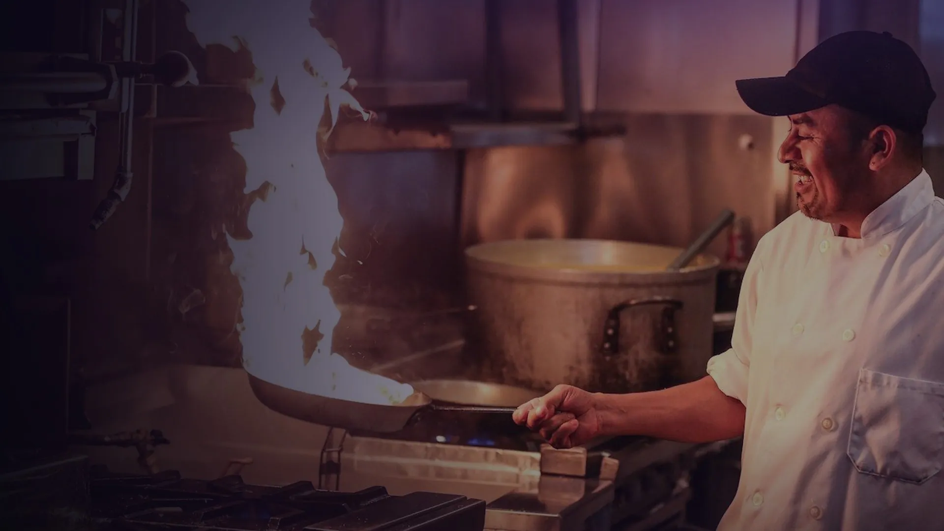 A chef tossing a flaming pan in the kitchen